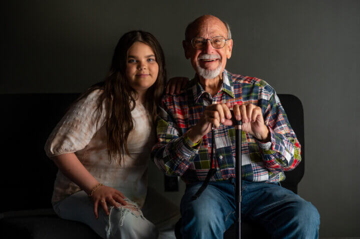 An LGBTQ+ young person and her grandfather smile at the camera.