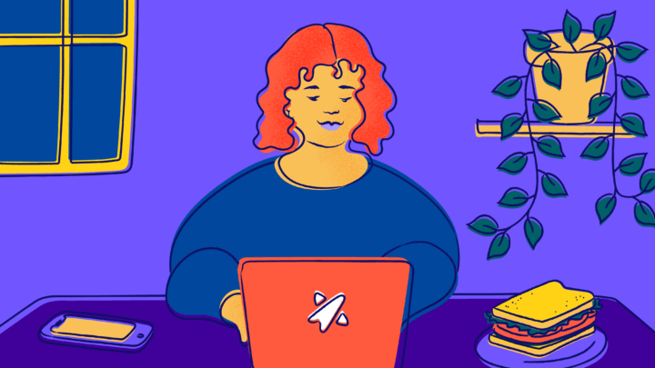 Smiling young female-presenting person sitting at a desk working on a computer.