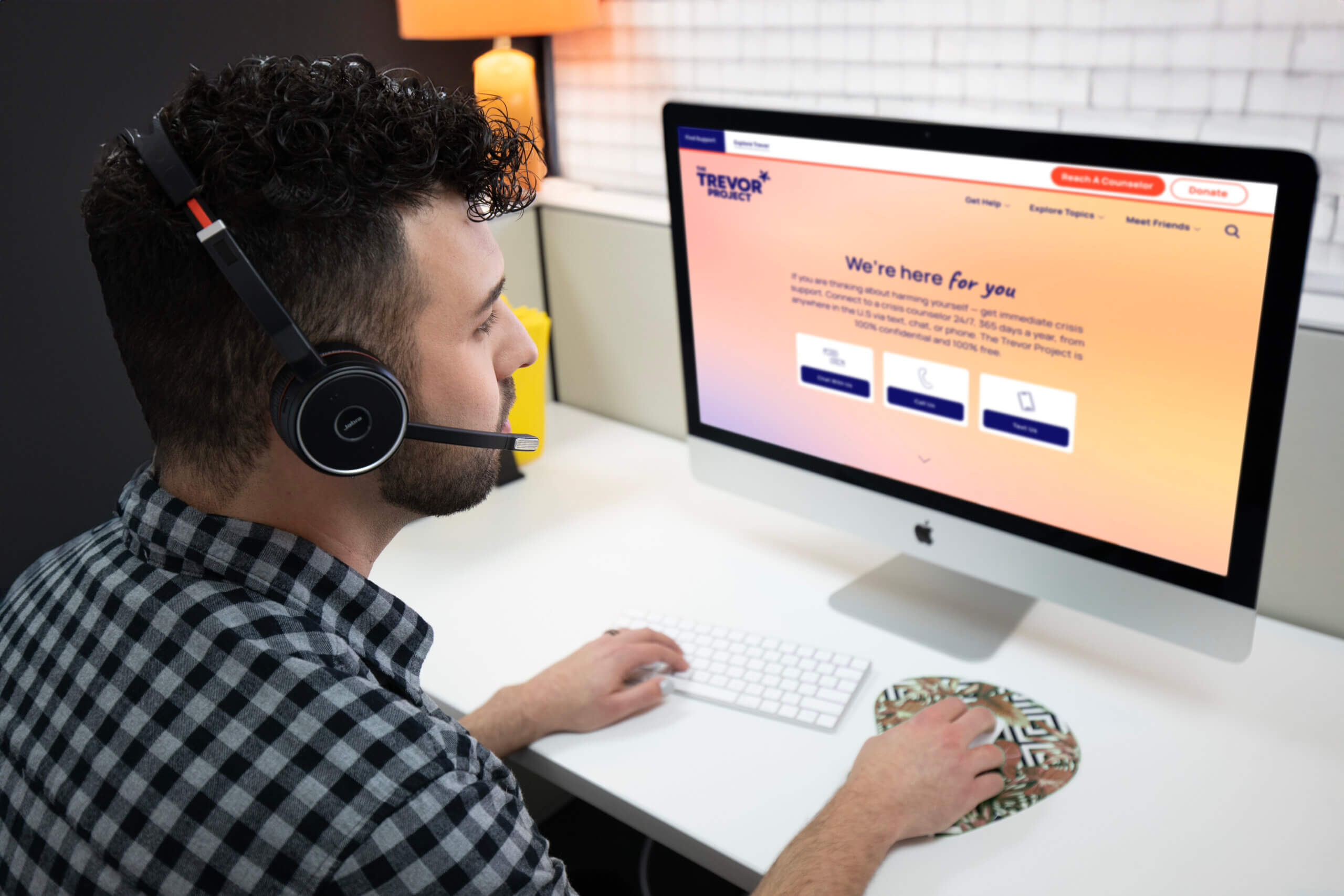 A Trevor volunteer wearing a headset, sits at a computer showing The Trevor Project's website.